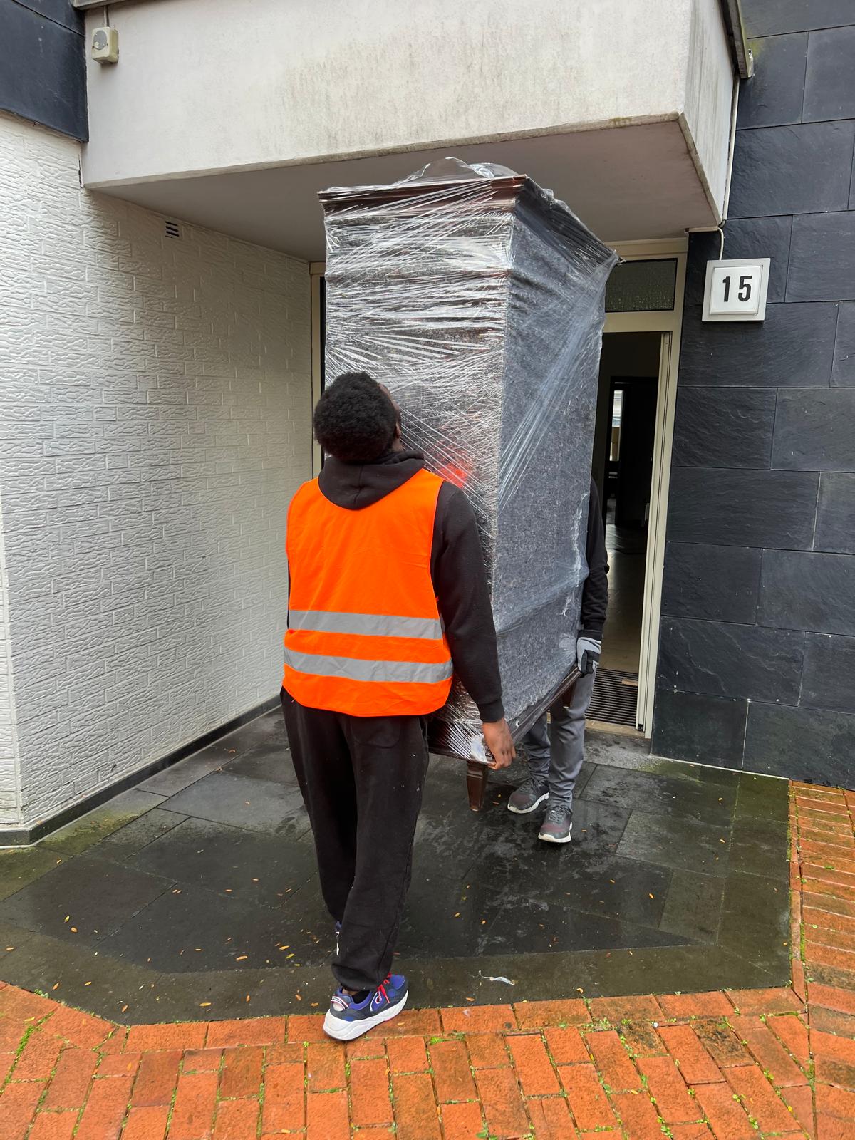 Zwei Möbelpacker tragen einen eingepackten Schrank
